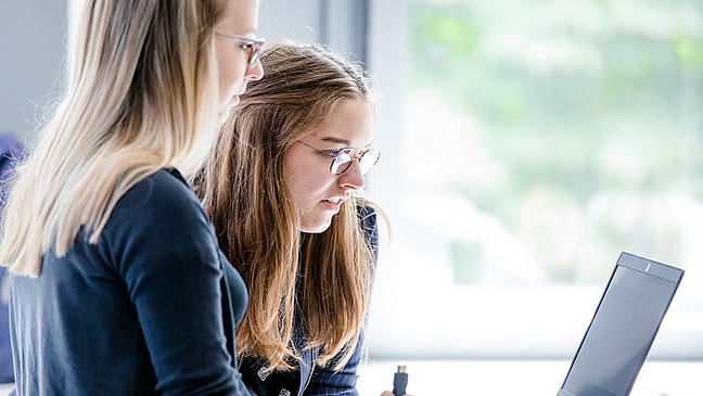 dekoratives Bild auf dem zwei weibliche Personen zusammen an einem Laptop arbeiten