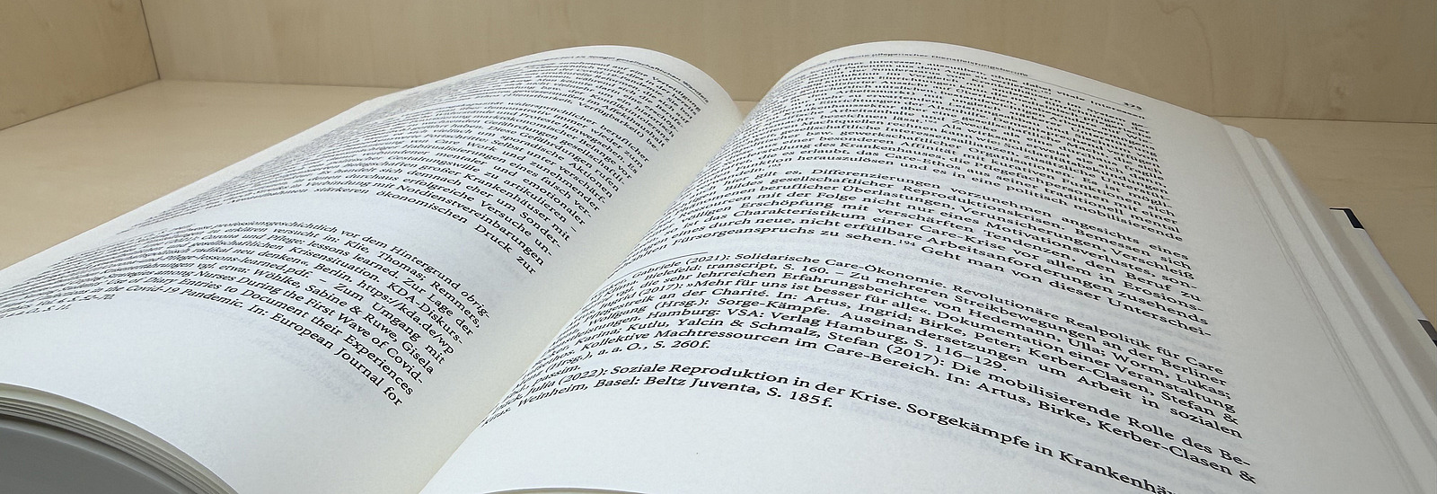 Ein aufgeschlagenes Buch liegt auf dem Regalboden; die Seiten sind leicht gew&ouml;lbt und zeigen dicht gesetzten Text in deutscher Sprache.