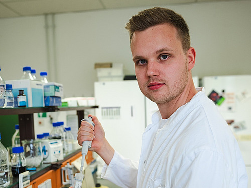 A man stands in the laboratory holding a pipette