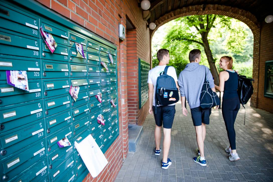 Drei Studierende laufen durch den Toreingang des Wohnheimes Jahnplatz vorbei an den Briefkästen.