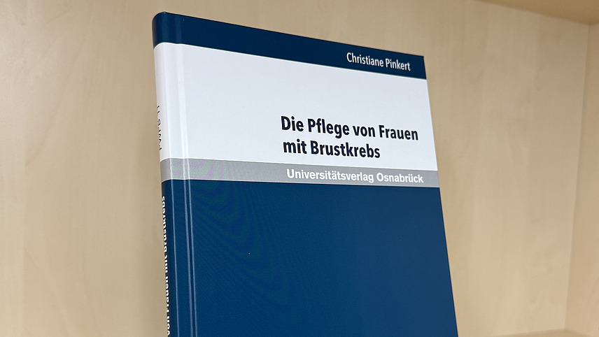 Ein Fachbuch von Christiane Pinkert mit dem Titel "Die Pflege von Frauen mit Brustkrebs" steht in einem Regal.