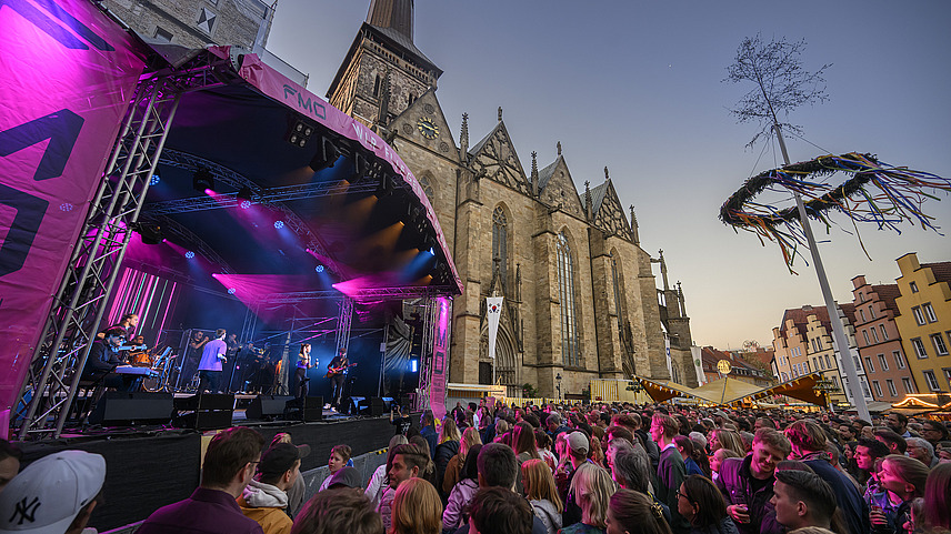 Several musicians on a stage in front of a church, audience in front of the stage