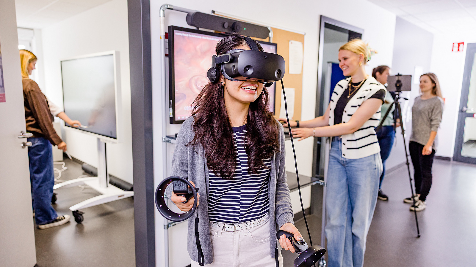 Eine Studierende tr&auml;gt eine Virtual Reality Brille. Im Hintergrund ist eine weitere Studierende zu sehen, welche die Simualtion &uuml;berwacht.