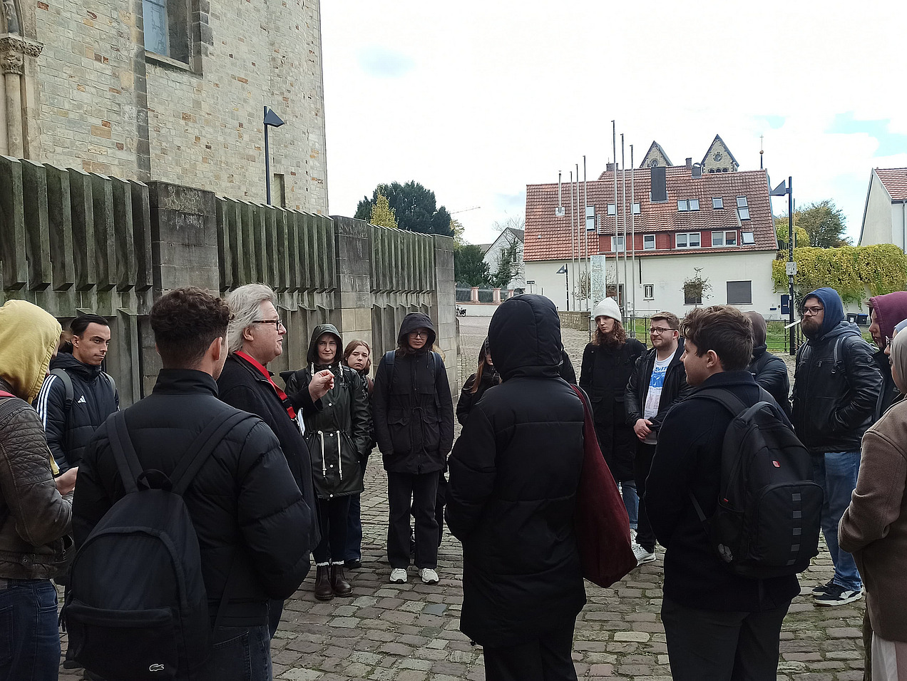 Das Bild zeigt eine Gruppe draußen vor einer Kirche in einem Halbkreis. In der Mitte steht ein Mann mit weißen Haaren. 