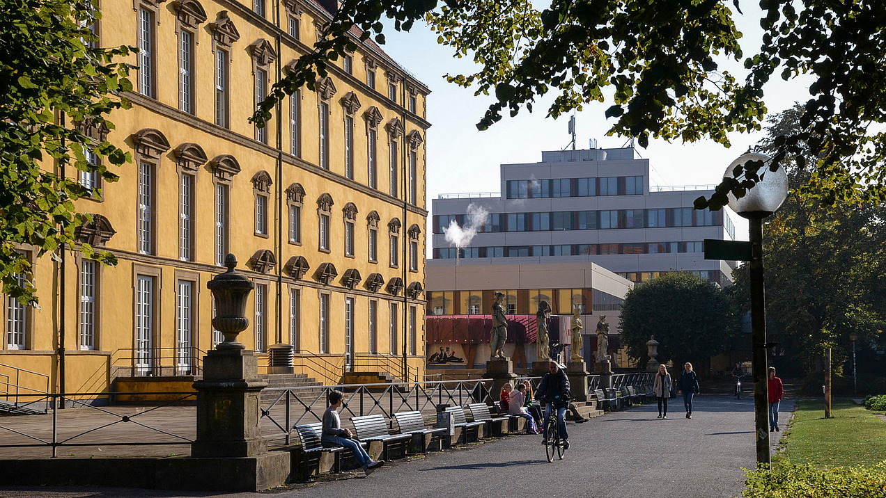 Seitliche Ansicht vom Gehweg zwischen Schloss und Schlossgarten. Beim Aufgang zur Terasse vor dem Schloss stehen vier Statuen aus Stein.