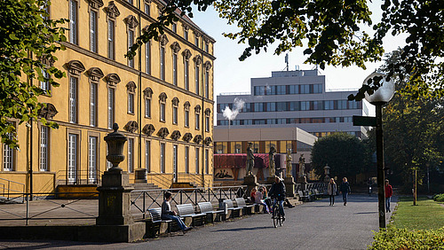 Seitliche Ansicht vom Gehweg zwischen Schloss und Schlossgarten. Beim Aufgang zur Terasse vor dem Schloss stehen vier Statuen aus Stein.