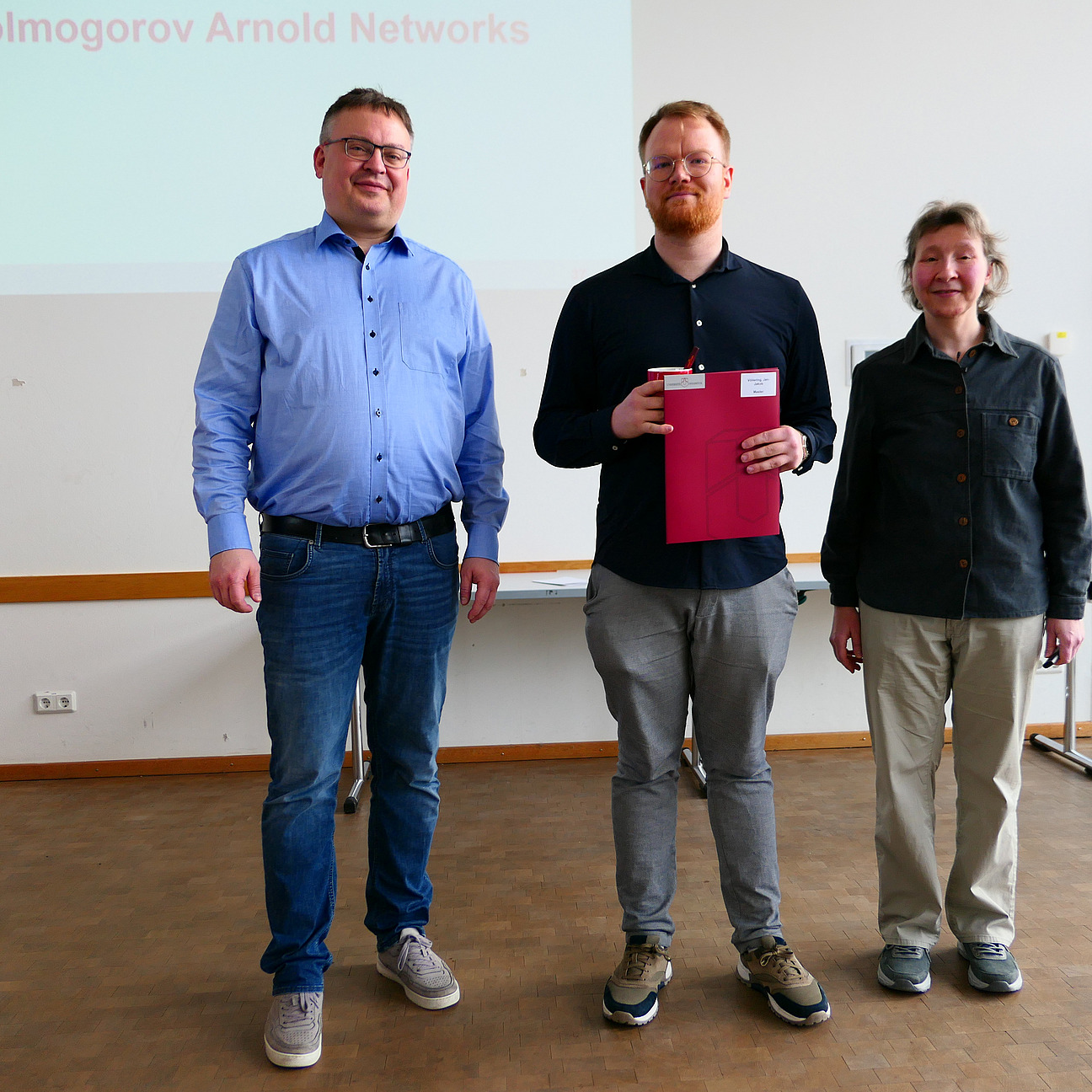 Ein Student steht mit seinem Abschlusszeugnis zwischen Dekan und Studiendekanin.