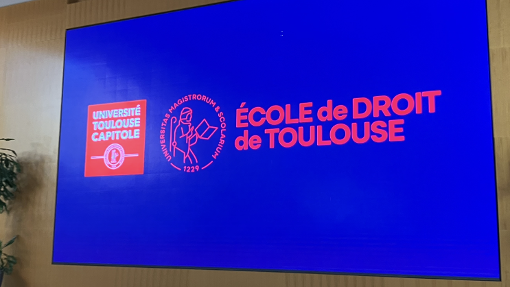 Auf Wandbildschirm blauer Hintergrund mit rotem Logo und Schriftzug "École de Droit de Toulouse"