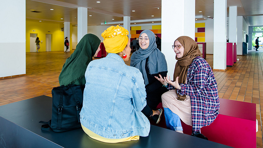 Four women wearing headscarves sit in a lounge area of the library on Westerberg and talk.