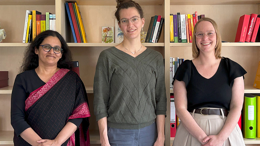 Drei Frauen stehen vor Bücherregalen