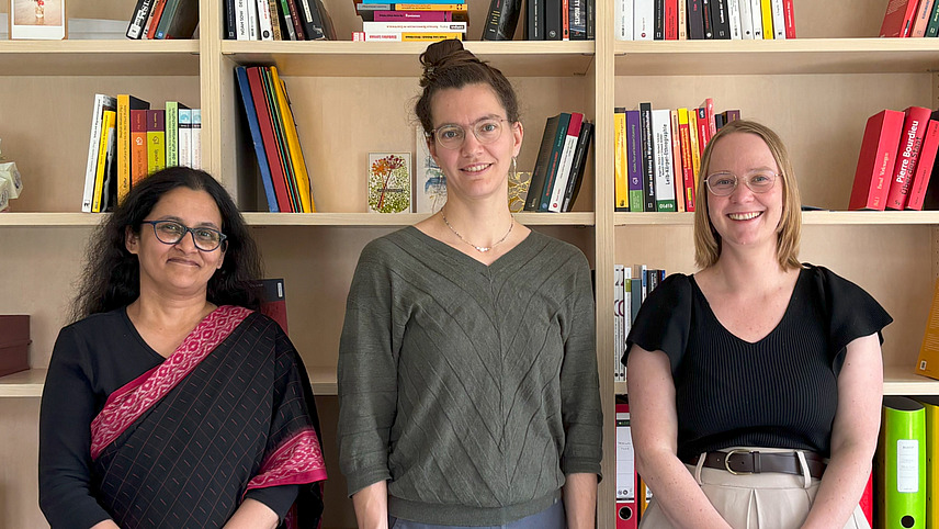 Drei Frauen stehen vor Bücherregalen