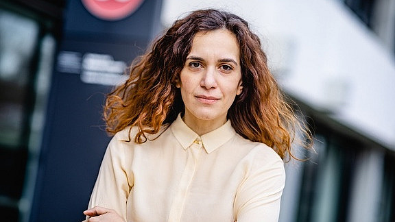 young woman with long dark curly hair looks friendly into the camera
