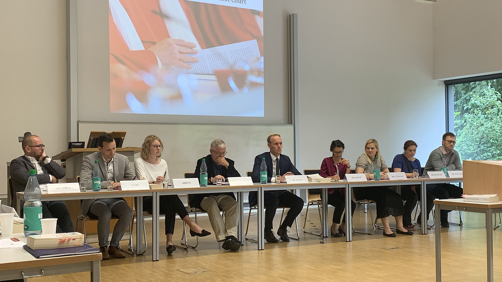 Tischreihe mit 5 sitzenden M&auml;nnern und 3 Frauen, die als "Richter" fungieren