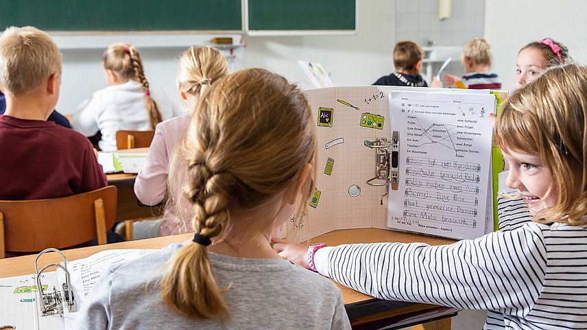 Zwei Schülerinnen sitzen an einem Tisch und tauschen sich über eine wortreich Aufgabe aus.