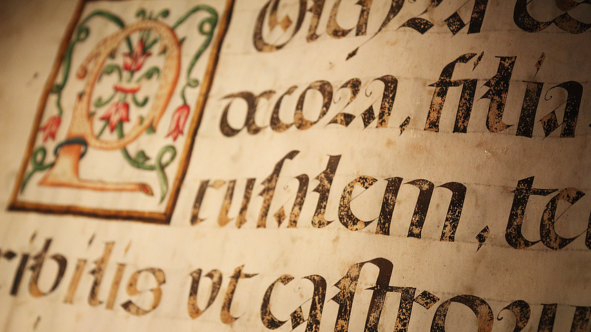 Close-up of an old book with Latin text and an ornate drawing.