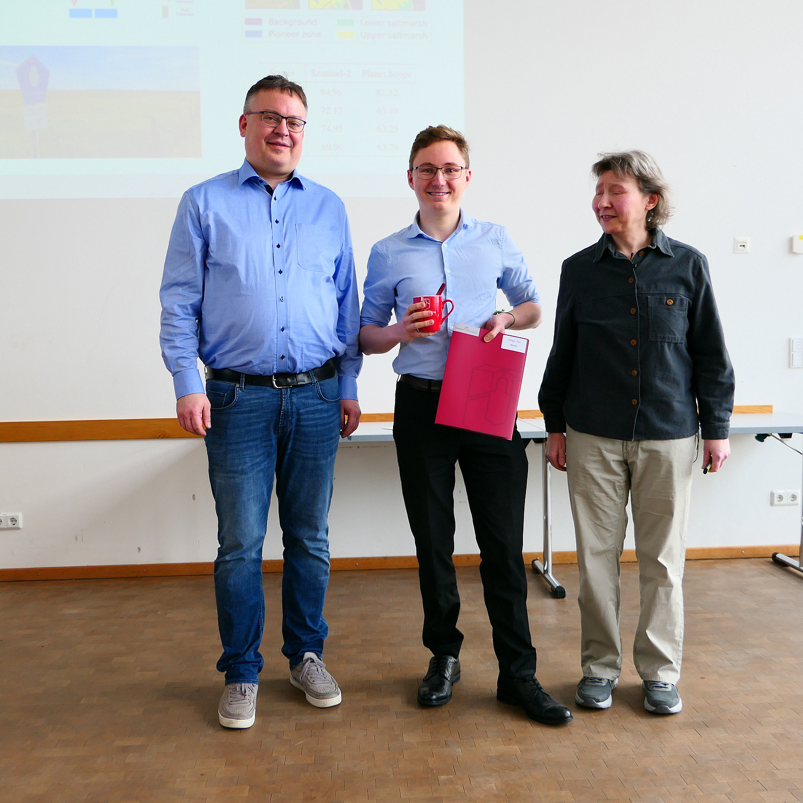 Ein Student steht mit seinem Abschlusszeugnis zwischen Dekan und Studiendekanin.