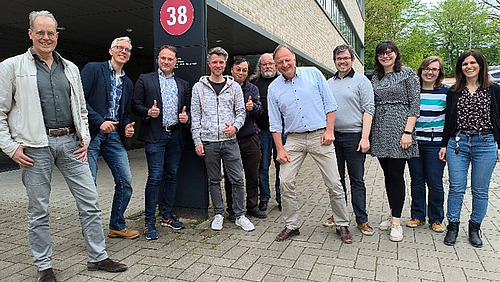 Eine Gruppe von Personen steht vor einem Geb&auml;ude und l&auml;chelt fr&ouml;hlich in die Kamera