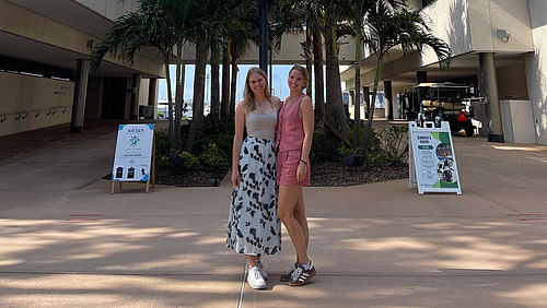 Alessa Gravemann und Fiona Latzel stehen in Florida vor einer USA-Flagge.