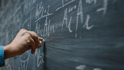Jemand schreibt Formeln an eine Tafel; Someone is writing formulas on a board.