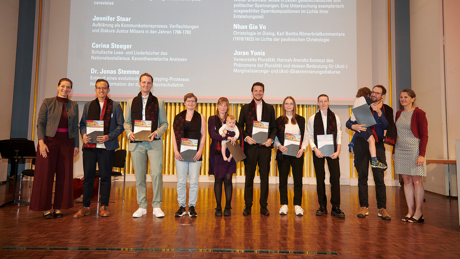 Several people stand on a stage, holding certificates in their hands and smiling into the camera