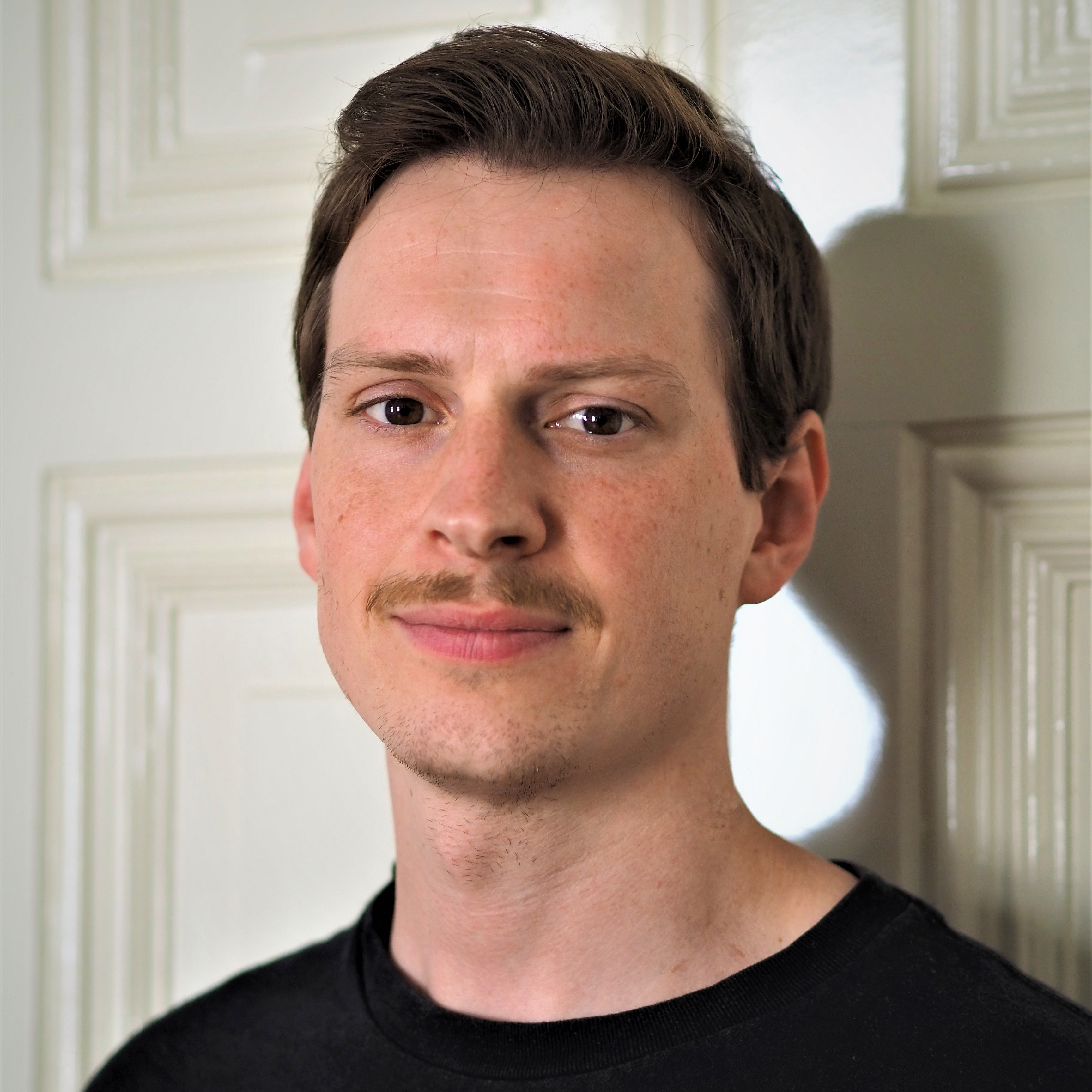 Dr. Benjamin B&uuml;scher steht vor einer wei&szlig;en T&uuml;r.