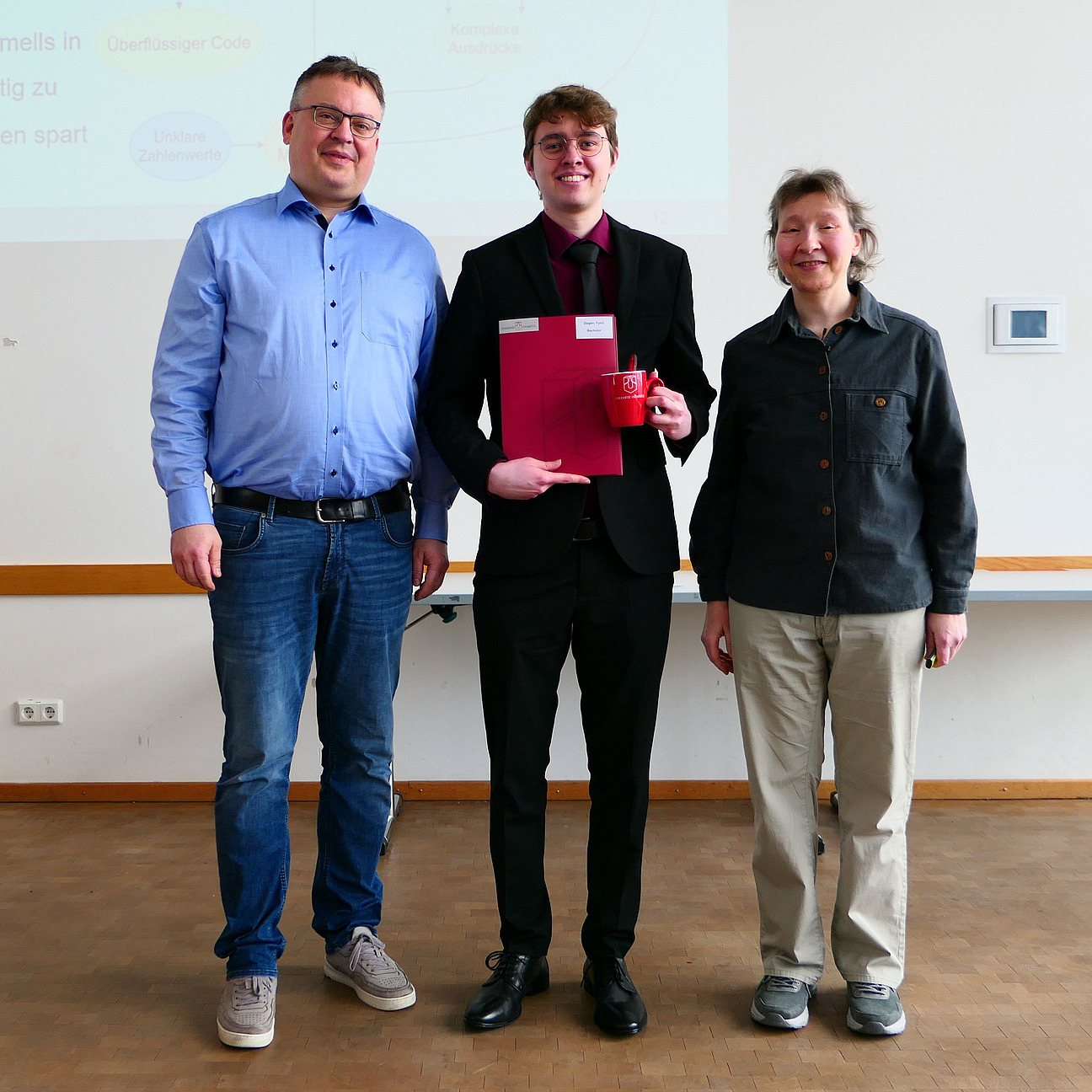 Ein Student steht mit seinem Abschlusszeugnis zwischen Dekan und Studiendekanin.
