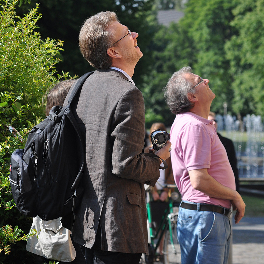 Prof. Dr. Helms ist im Profil zu sehen, er steht vor einer Hecke am Osnabrücker Schloss und schaut nach oben, neben udn vor ihm sind zwei weitere Personen zu sehen, die nach oben schauen.