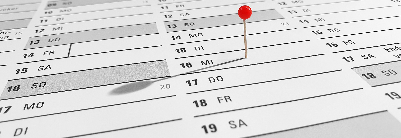 Nahaufnahme von einem Kalender aus einem sehr niedrigen Winkel. Eine einzelne, rote Pinnadel ist auf einen Tag gesteckt.