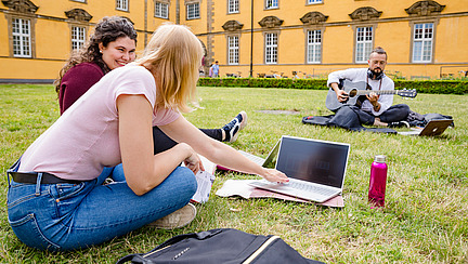 Three students are sitting together in the castle courtyard. One of them is playing the guitar.
