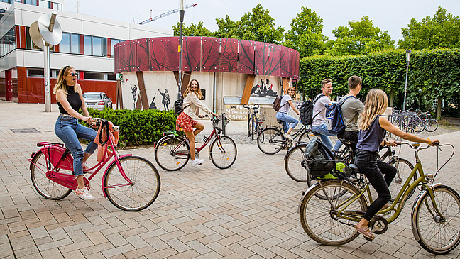 Eine Gruppe Studierender fährt mit ihren Fahrrädern neben dem Schloss.