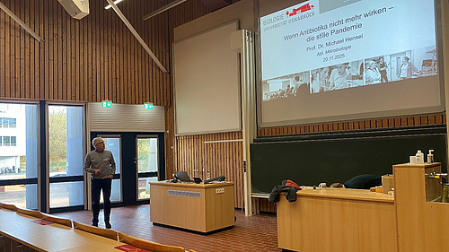 A man is standing in a lecture hall holding a pointer in his hand.