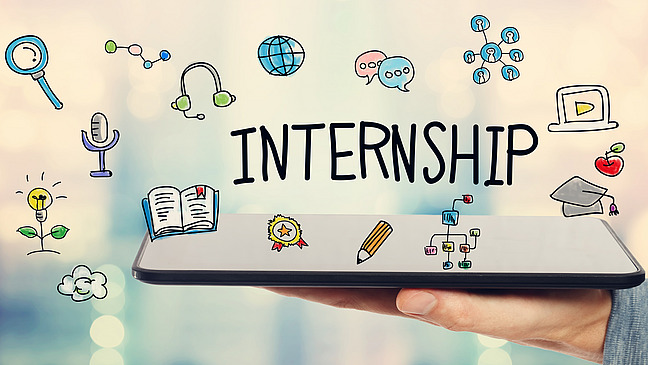 Hand h&auml;lt ein offenes Buch. Auf dem Bild wurde manuell das Wort "INTERNSHIP" eingetragen und dazu Icons skizziert, die mit der Vorbereitung eines Praktikums in Verbindung stehen.