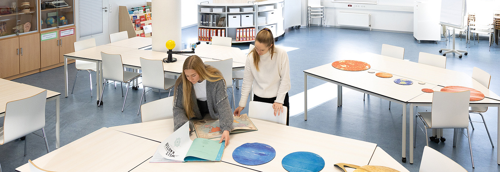Zwei Studentinnen sitzen an einem Tisch in einer Lernwerkstatt und arbeiten mit Material zum geographischen Lernen.
