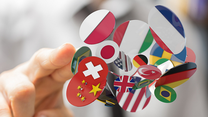 Eine Hand zeigt auf ganz viele kleine Flaggen der ganzen Welt.