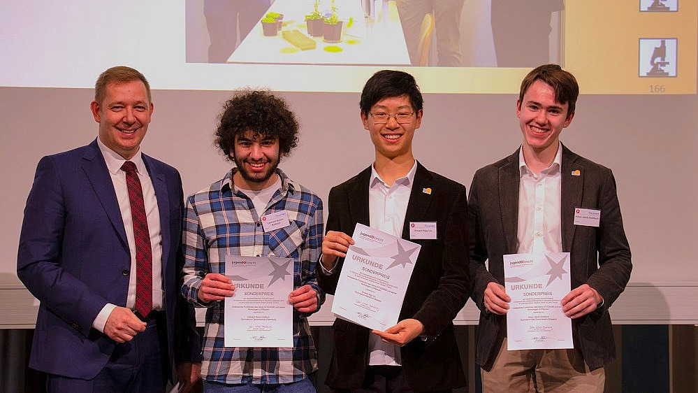 Vier M&auml;nner l&auml;cheln in die Kamera, die drei j&uuml;ngeren halten Urkunden in den H&auml;nden