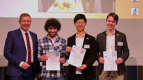 Vier M&auml;nner l&auml;cheln in die Kamera, die drei j&uuml;ngeren halten Urkunden in den H&auml;nden