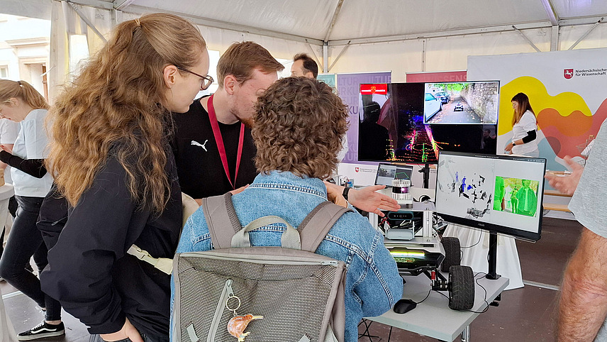 People viewing a 3D display on a screen under a pavilion.