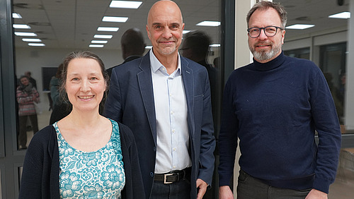 Eine Frau und zwei M&auml;nner schauen in die Kamera.