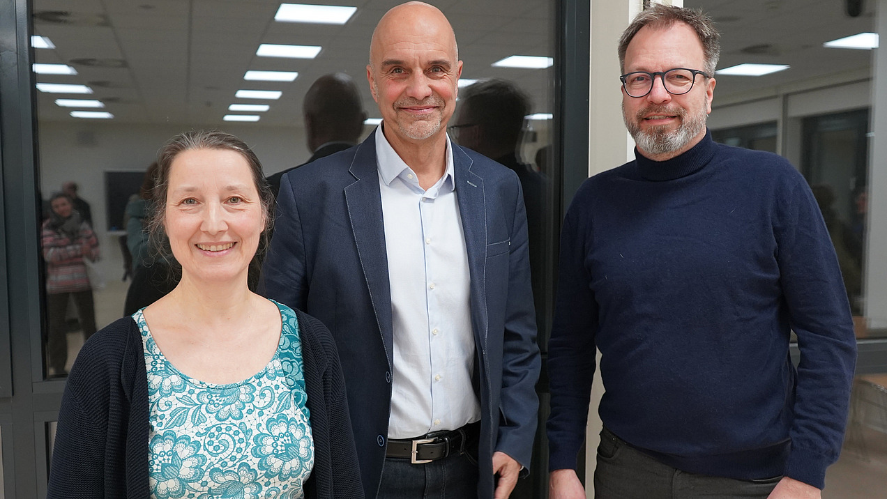 Eine Frau und zwei M&auml;nner schauen in die Kamera.