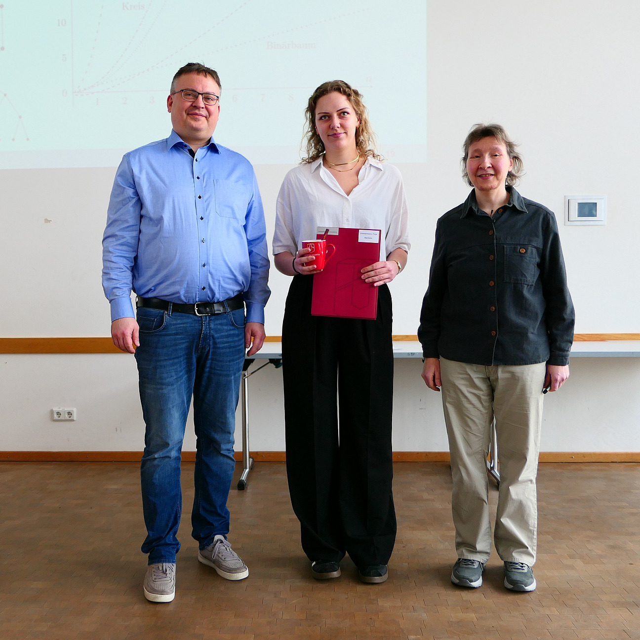 Eine Studentin steht mit ihrem Abschlusszeugnis zwischen Dekan und Studiendekanin.