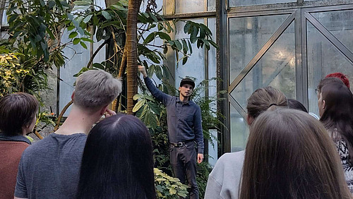 Personen stehen im Regenwaldhaus des Botanischen Gartens und schauen auf einen Mann, der offenbar etwas erkl&auml;rt.