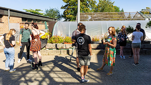 Personen stehen auf einer gepflasterten Fl&auml;che und unterhalten sich.