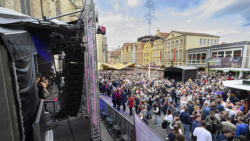 A stage with many spectators in front of it, buildings in the background