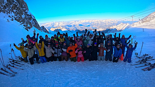 Gruppe Skifahrer mir Ausr&uuml;stung, hebt die Arme im Schnee auf einem Berg.