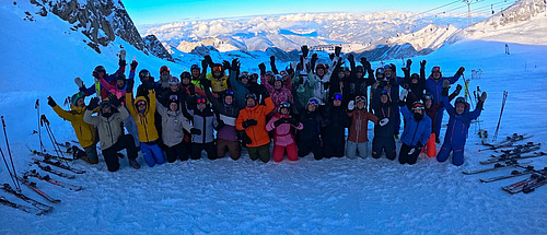 Gruppe Skifahrer mir Ausr&uuml;stung, hebt die Arme im Schnee auf einem Berg.