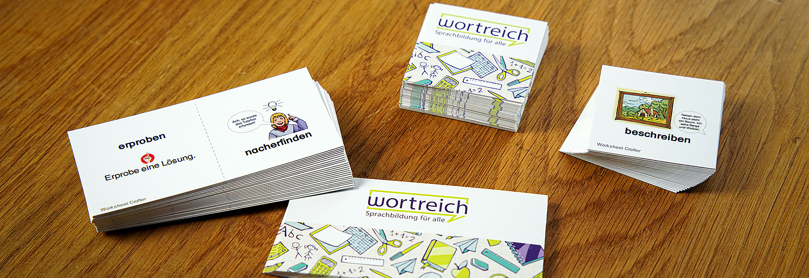 Zwei Wortreich-Spiele liegen auf einem Tisch. Es handelt sich um ein Memoryspiel und ein Dominospiel zum Anlegen. Man erkennt folgende Wörter: erproben, nacherfinden, beschreiben.