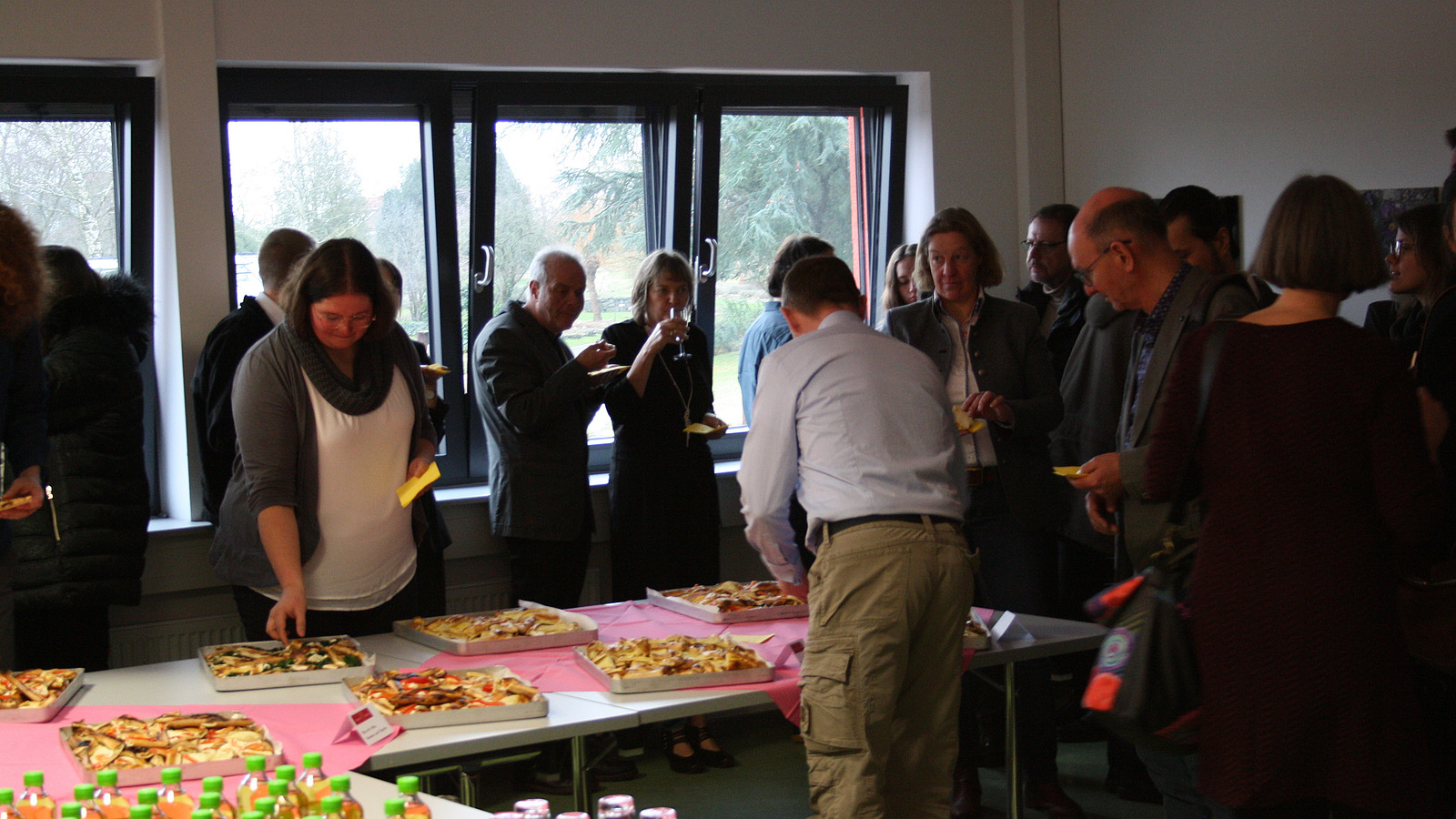 ../Download/Febr2024/IMG_7857.JPG Several people stand in front of and behind a table with finger food.