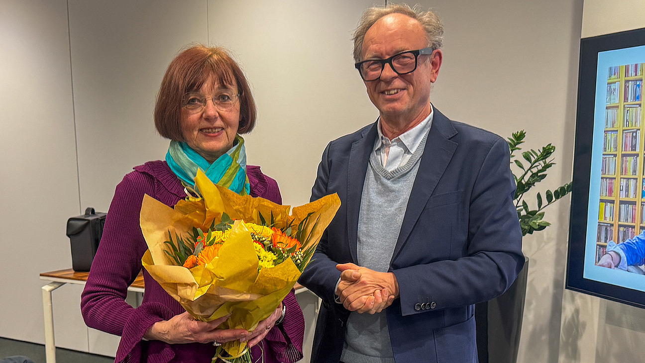 Ein Mann und eine Frau schauen in die Kamera, die Frau h&auml;lt einen Blumenstrau&szlig; in der Hand