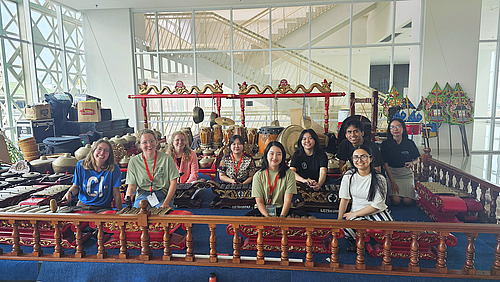 Eine Gruppe von Studierenden posiert vor einer traditionellen javanischen Gamelan-Anlage. Die Instrumente sind kunstvoll verziert und die Gruppe scheint eine kulturelle Erfahrung zu machen.