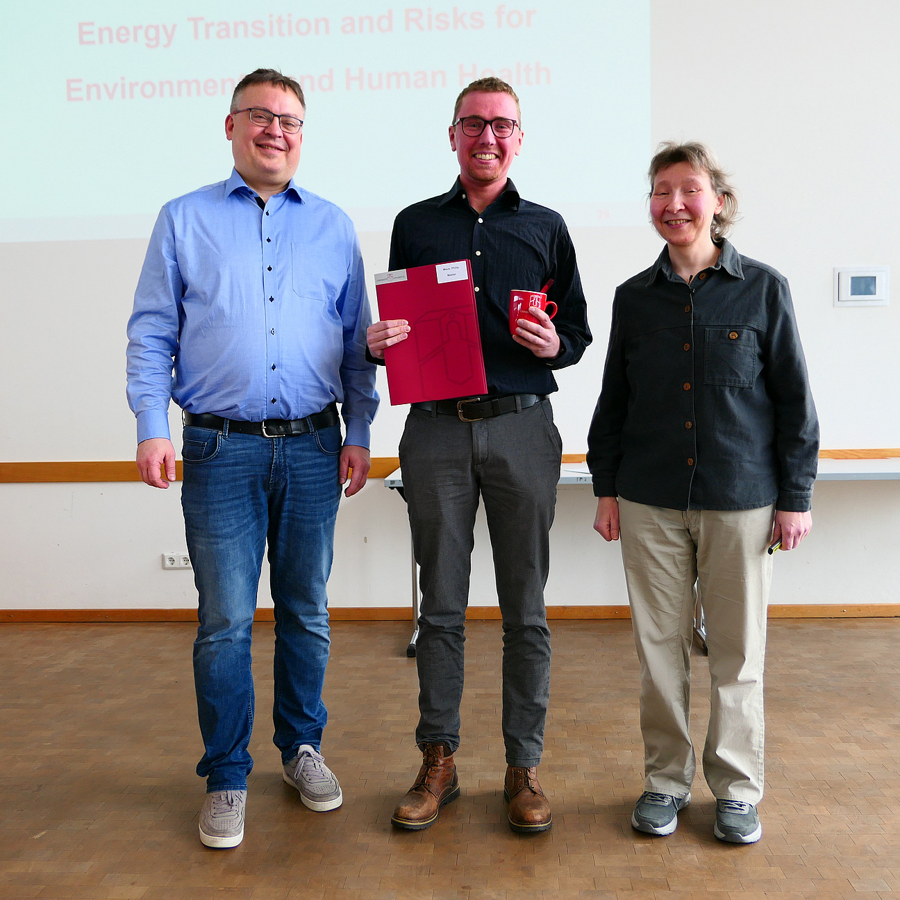 Ein Student steht mit seinem Abschlusszeugnis zwischen Dekan und Studiendekanin.